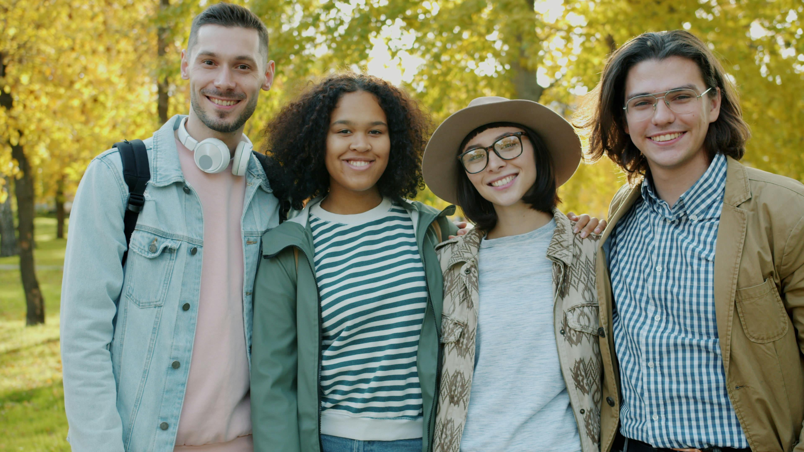 pexels-photo-36763393-36763393 Four friends smiling together in a park during a sunny fall day.